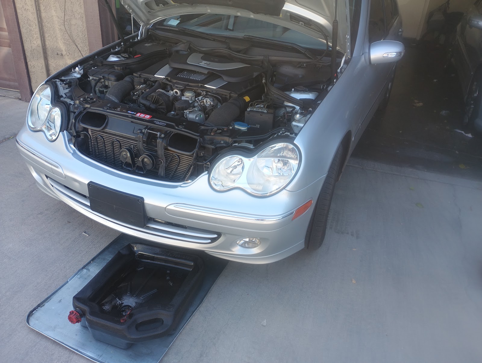Silver Mercedes-Benz C-class with hood open and oil drain pan positioned for an oil change