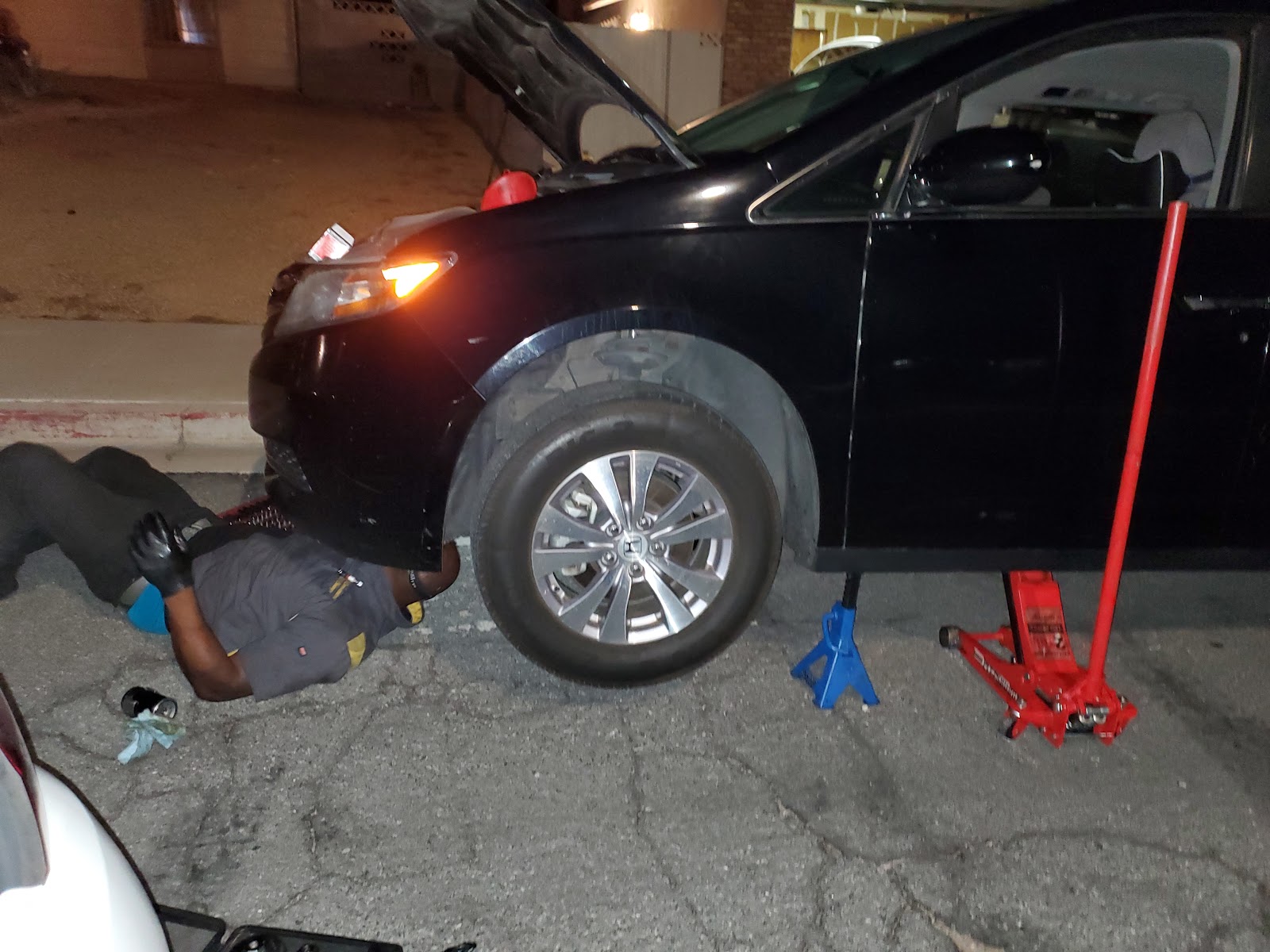 Mechanic lying under a black Honda raised on a jack stand at night